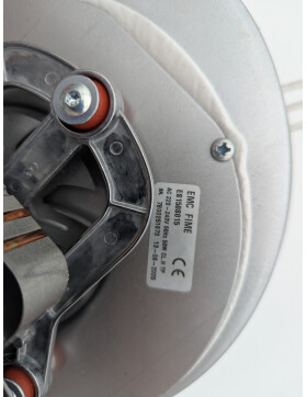 Unterseite eines MCZ-Abgasgebläses mit sichtbarem Motor und elektrischen Anschlüssen. Der Motor verfügt über eine schwarze Kunststoffabdeckung und eine kupferfarbene Wicklung. Die silberne Metallhalterung ist mit Schrauben befestigt, und im Hintergrund ist das Lüfterrad des Gebläses erkennbar. Ein Etikett mit technischen Angaben ist auf dem Gehäuse angebracht.